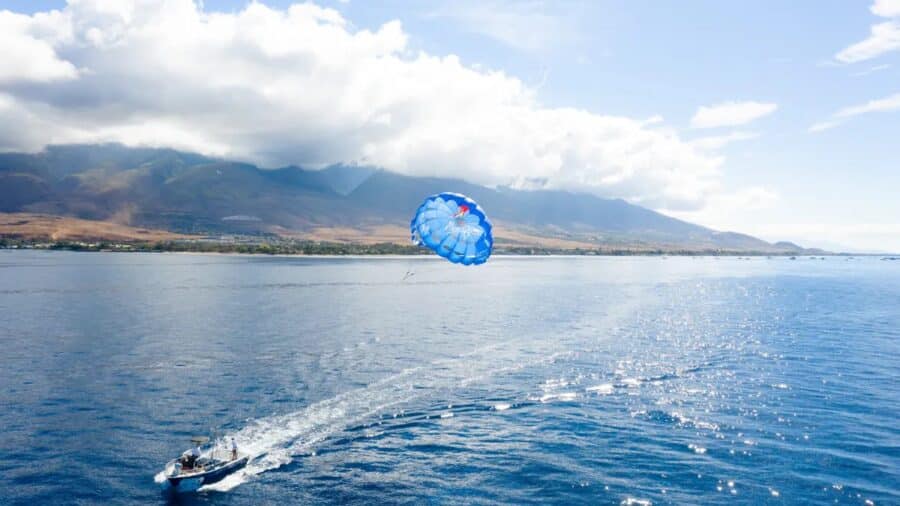 A UFO Parasail boat with an open parachute behind it and West Maui in the background